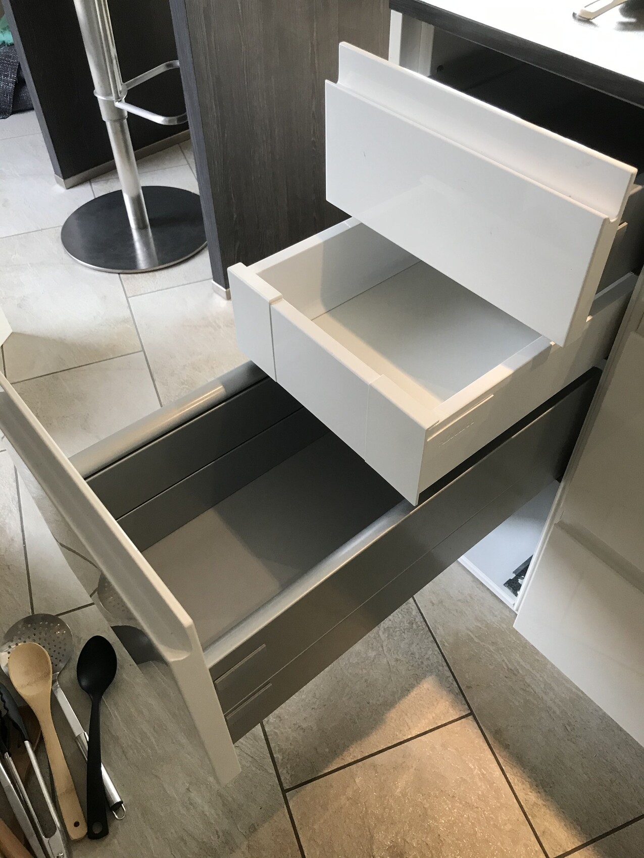Weiße Küchen-Schubladen offen; obere kleine, darunter größere; Werkzeuge auf dem Boden.