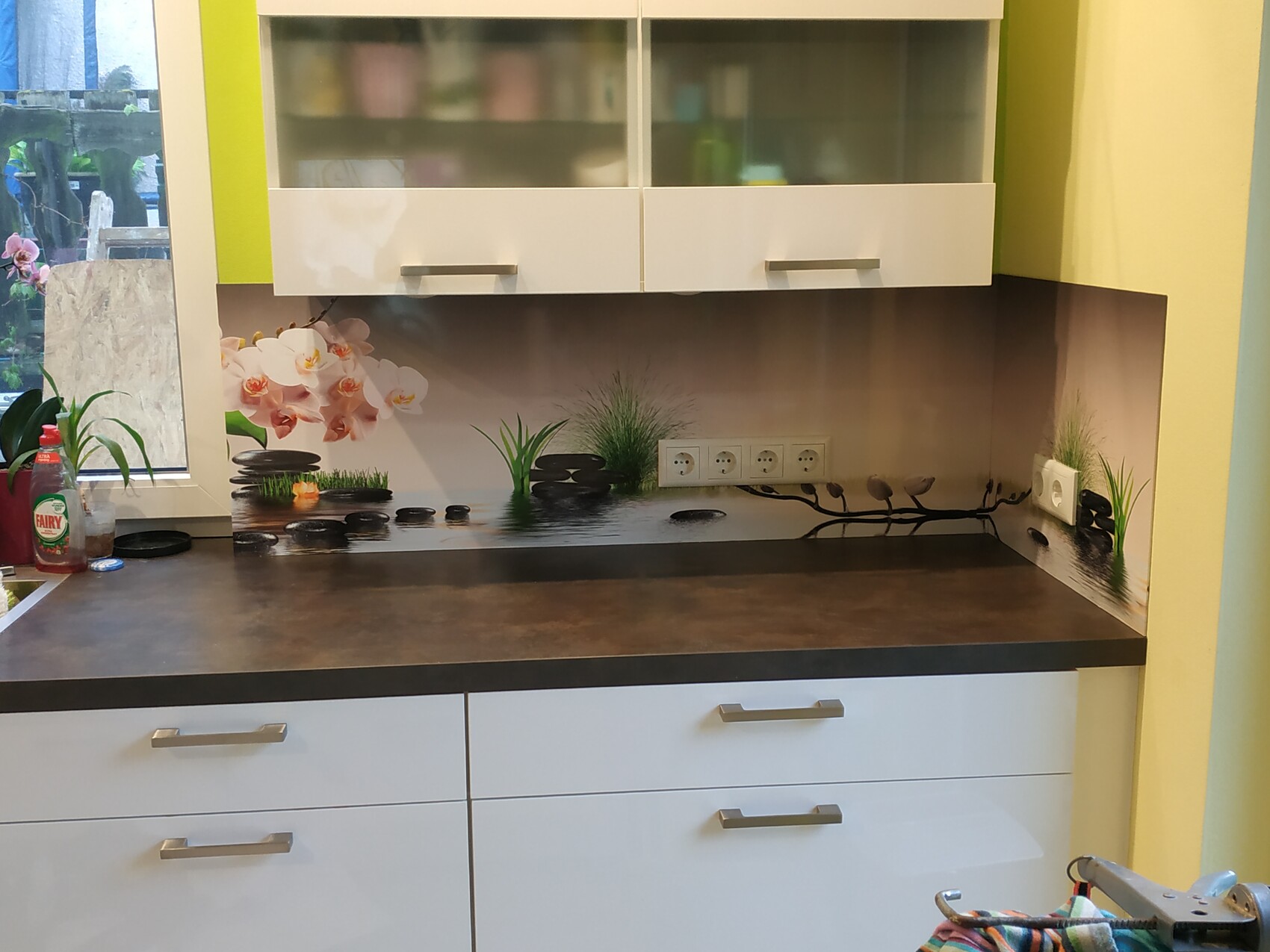 Moderne Küche: weiße Unterschränke, dunkle Arbeitsplatte, Rückwand mit Orchideenmotiv, Steinen.
