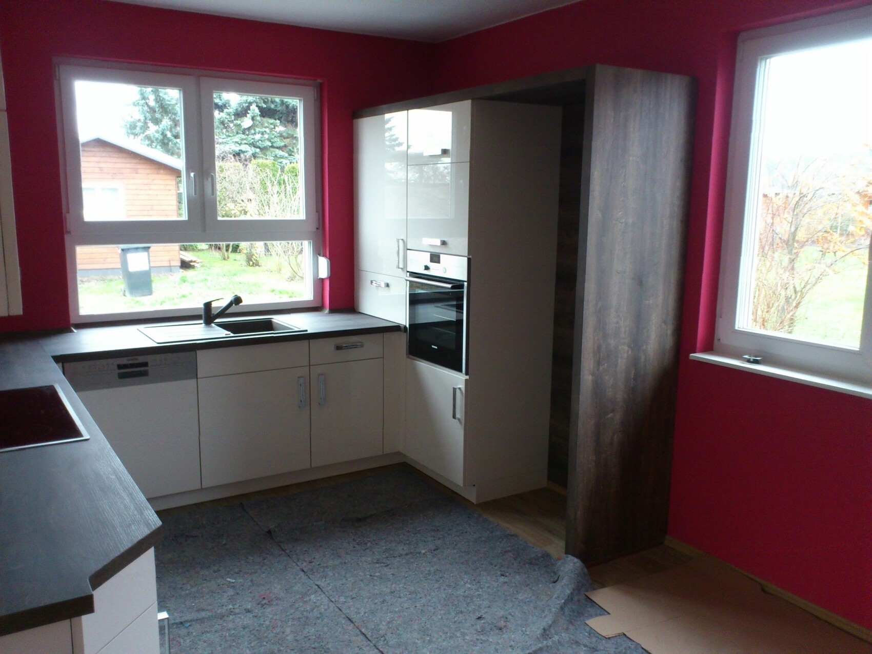 Moderne Küche mit weißen Fronten, Backofen, Spüle; pinke Wand, Fenster mit Gartenblick.