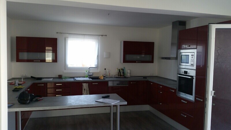 Moderne Küche mit roten Hochglanz-Schränken, Spüle unter dem Fenster, Insel und Backofen/Mikrowelle.