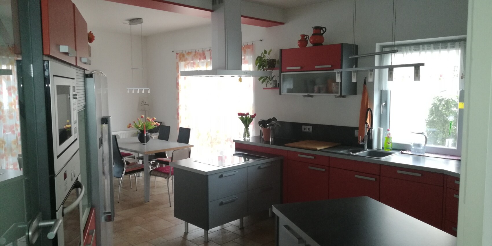 Moderne Küche mit roten Schränken, Kochinsel, Esstisch und Tulpen.