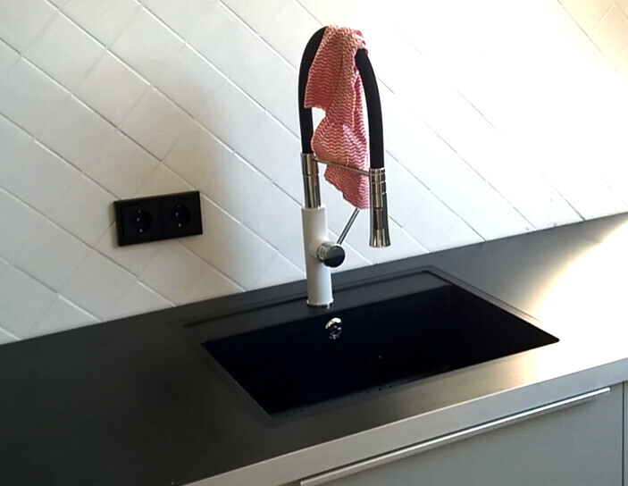 Moderne Küchenarmatur mit schwarzem Schlauch; pinkes Tuch hängt über dem Auslauf.