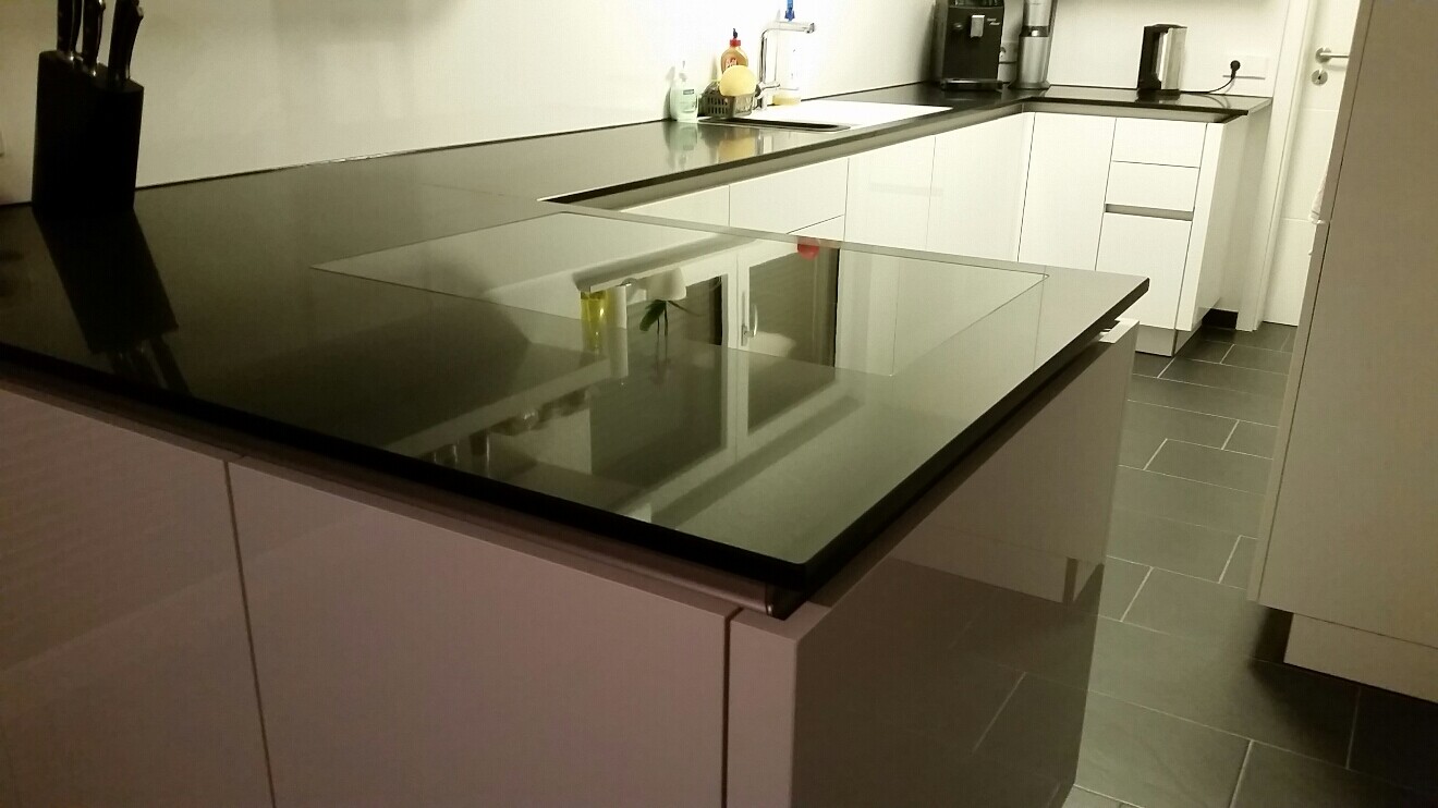 Moderne Küche mit dunkler Glas-Arbeitsplatte als Insel, weißen Schränken und dunklen Bodenfliesen.