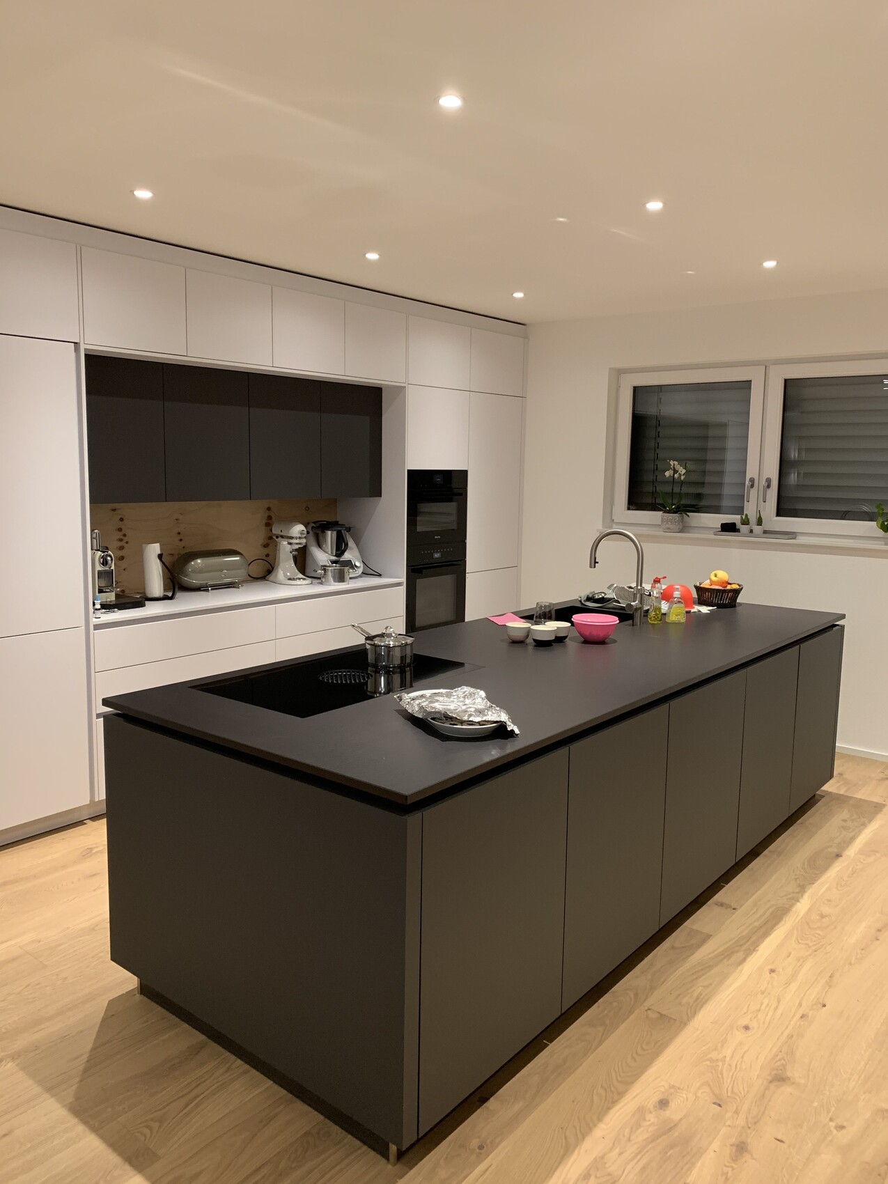 Moderne Küche mit dunkler Insel, weißen Schränken, Backofen, Spüle und Fenster mit Pflanzen