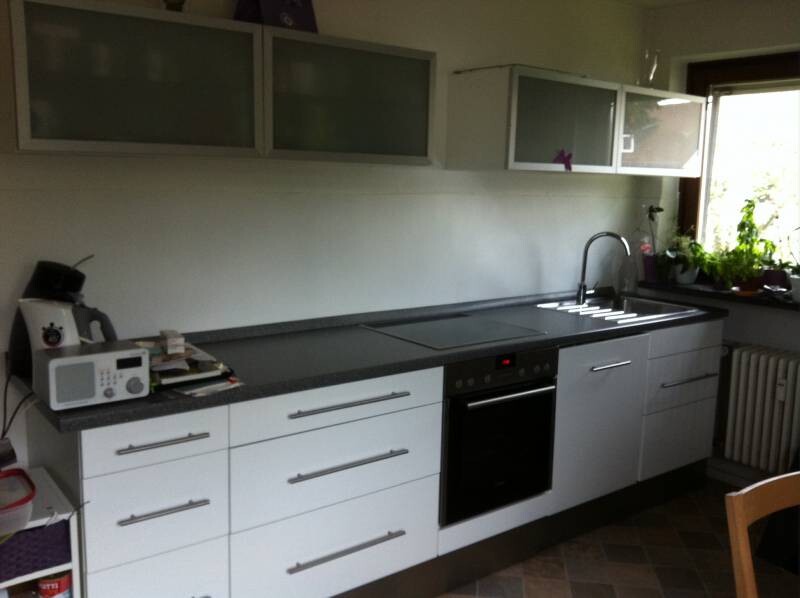 Moderne Küche mit weißen Fronten, dunkler Arbeitsplatte, Spüle und Backofen.
