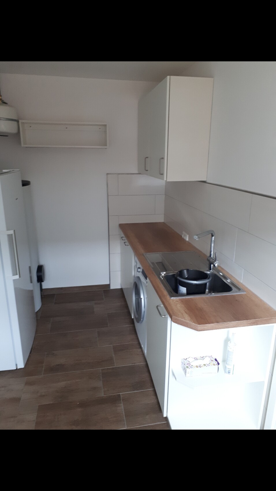 Schmale Küche mit Holz-Arbeitsplatte, Spüle, Waschmaschine, weißen Hängeschränken und Fliesen.