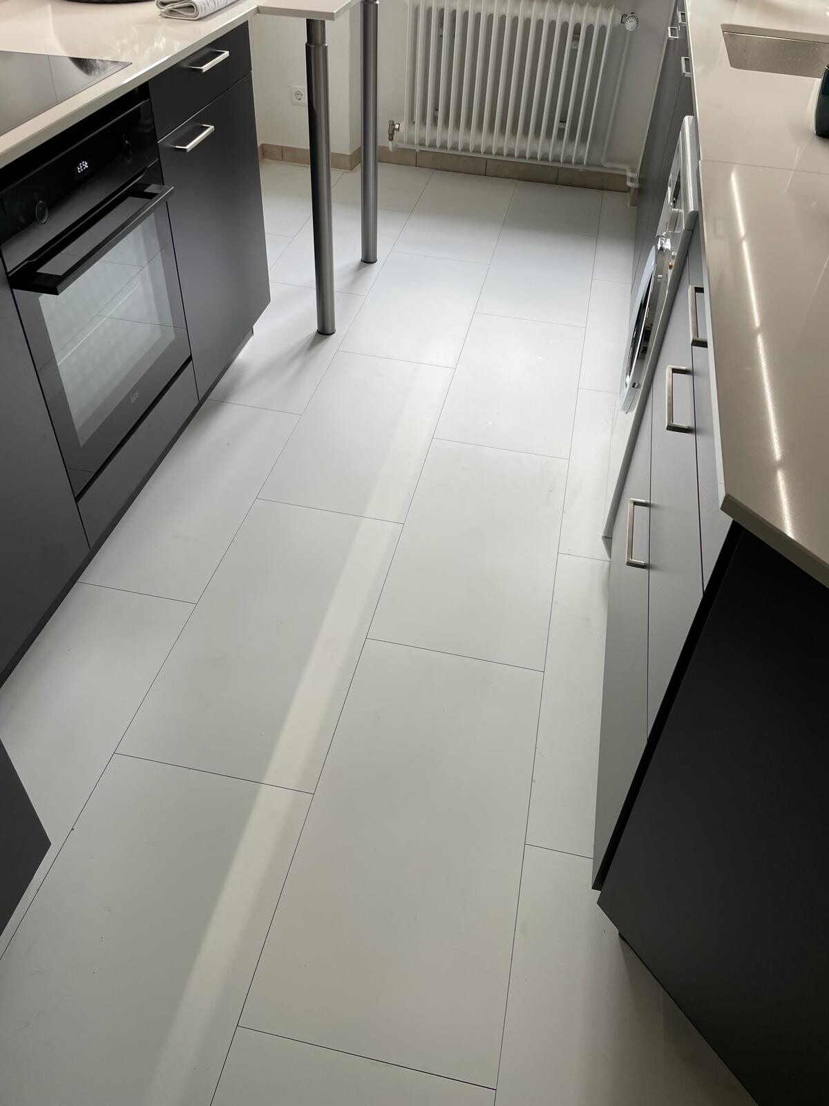 Moderne Küche mit weißen Fliesen, grauen Fronten, Backofen links, Waschmaschine rechts.