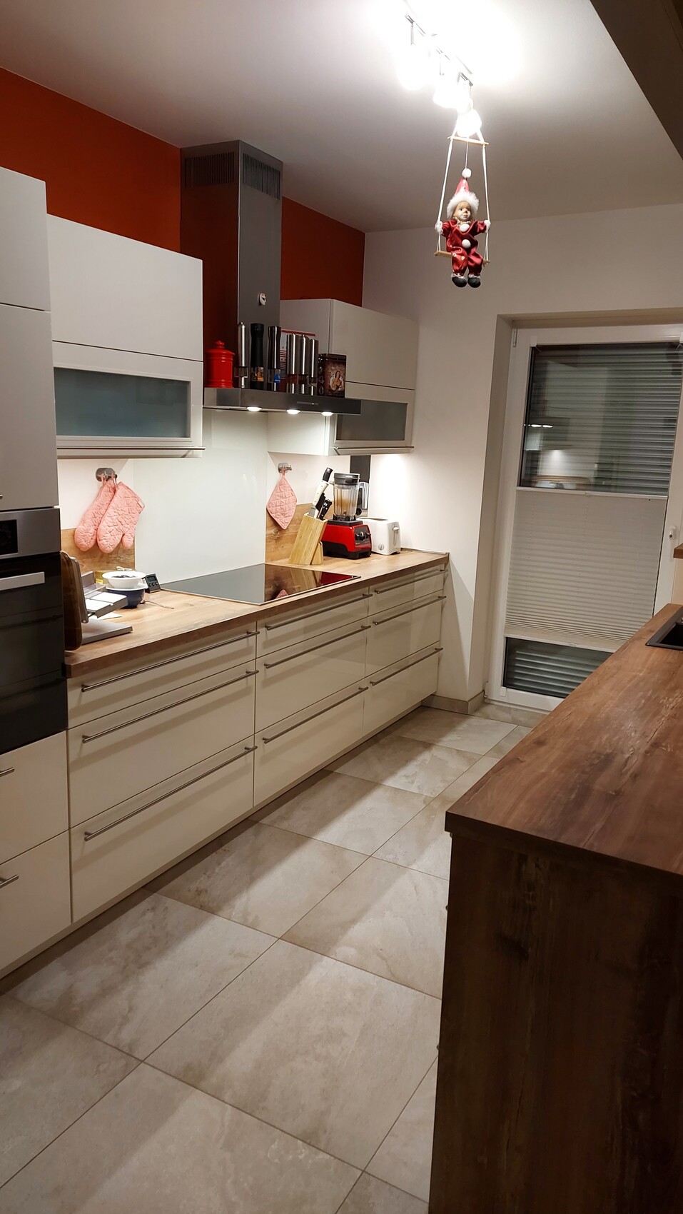 Moderne Küche: weiße Schränke, Holzplatte, rote Wand; Elf auf Schaukel hängt von Deckenleuchte.
