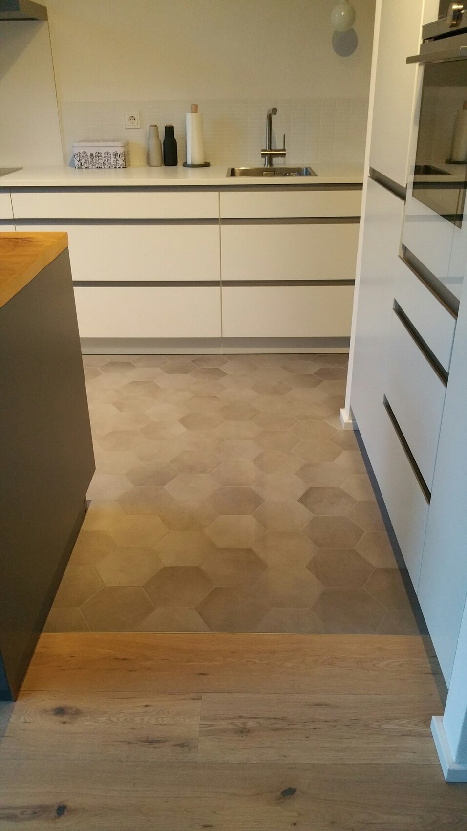 Moderne Küche mit weißen Schränken, Spüle, Armatur und grauen hexagonalen Bodenfliesen.