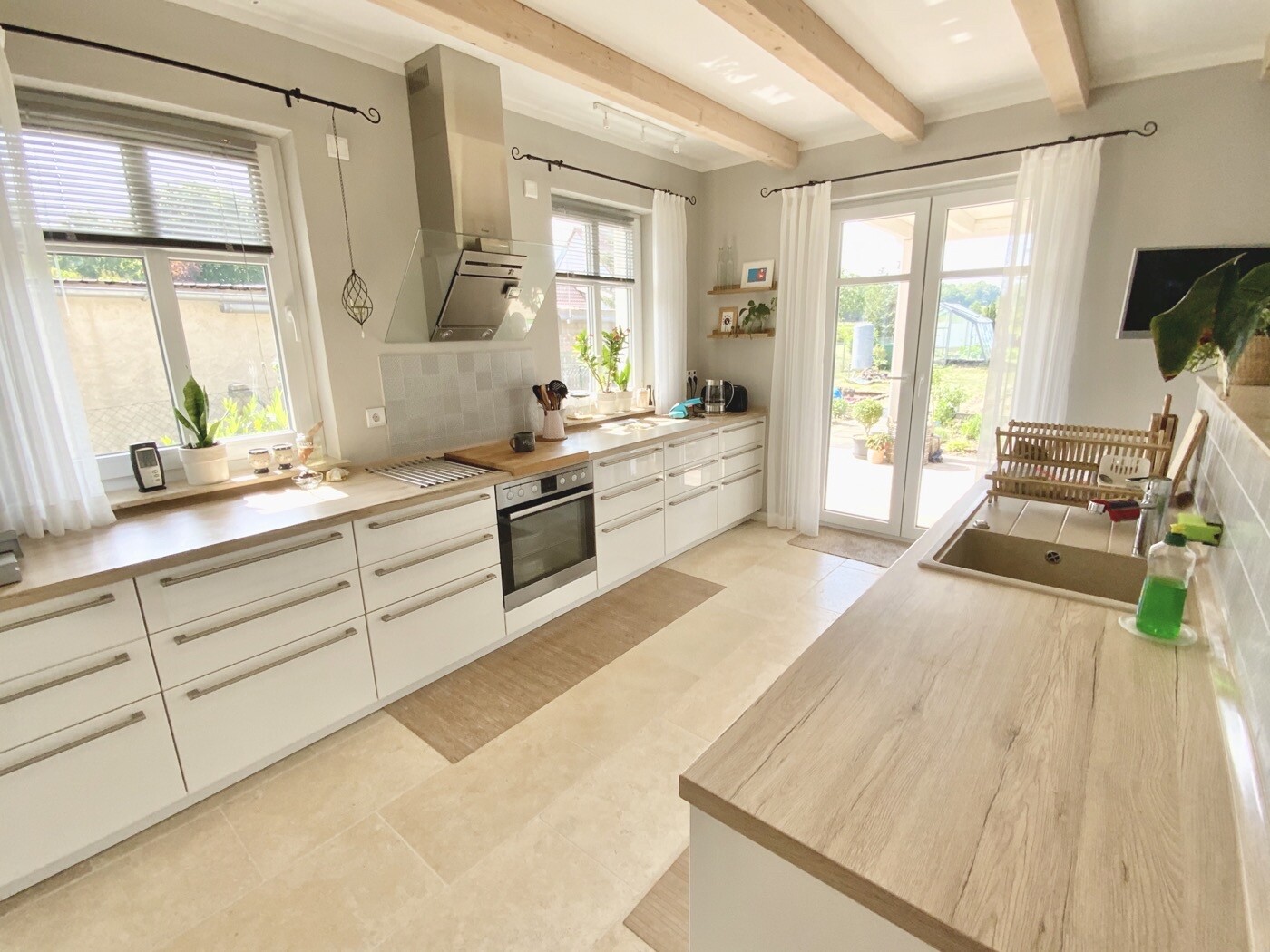 Helle Küche mit weißen Schränken, Holz-Arbeitsplatte, Herd, Fenster und Blick nach Garten.
