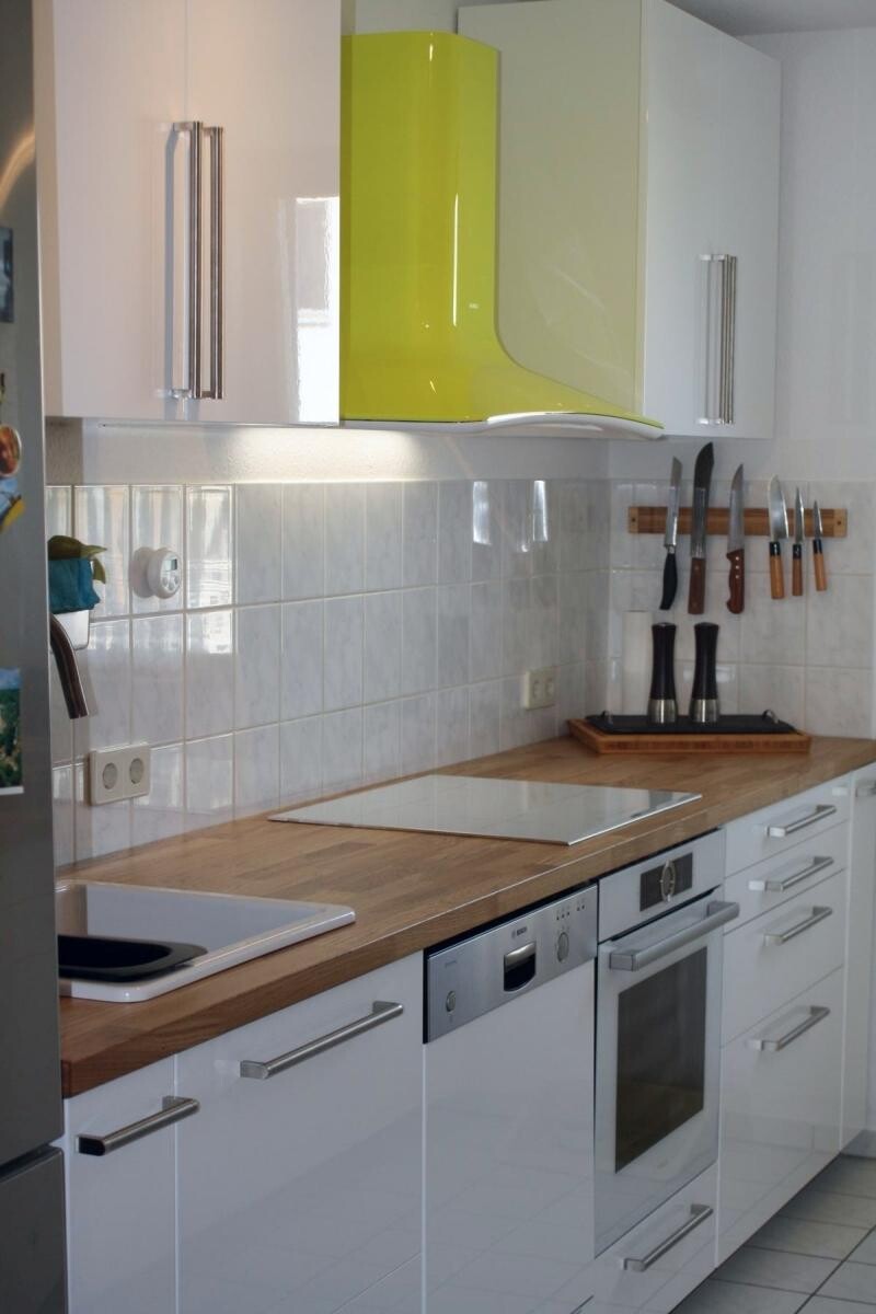 Moderne Küche mit weißen Oberflächen, Holz-Arbeitsplatte, Backofen und Messerleiste