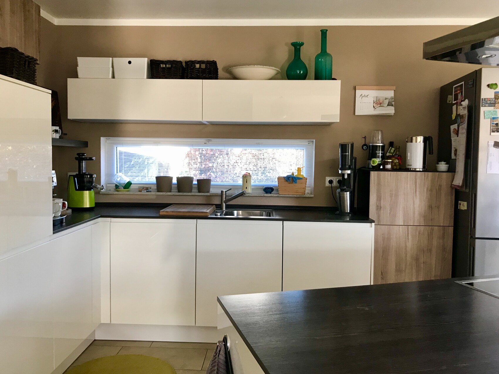 Moderne Küche mit weißen Schränken, dunkler Arbeitsplatte, Spüle am Fenster und grüne Glasvasen.