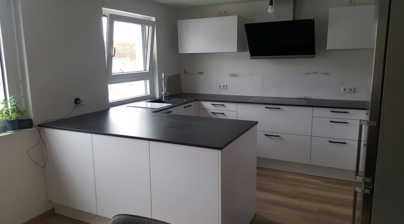 Moderne Küche mit weißen Schränken, schwarzer Arbeitsplatte, Kücheninsel und Spüle am Fenster