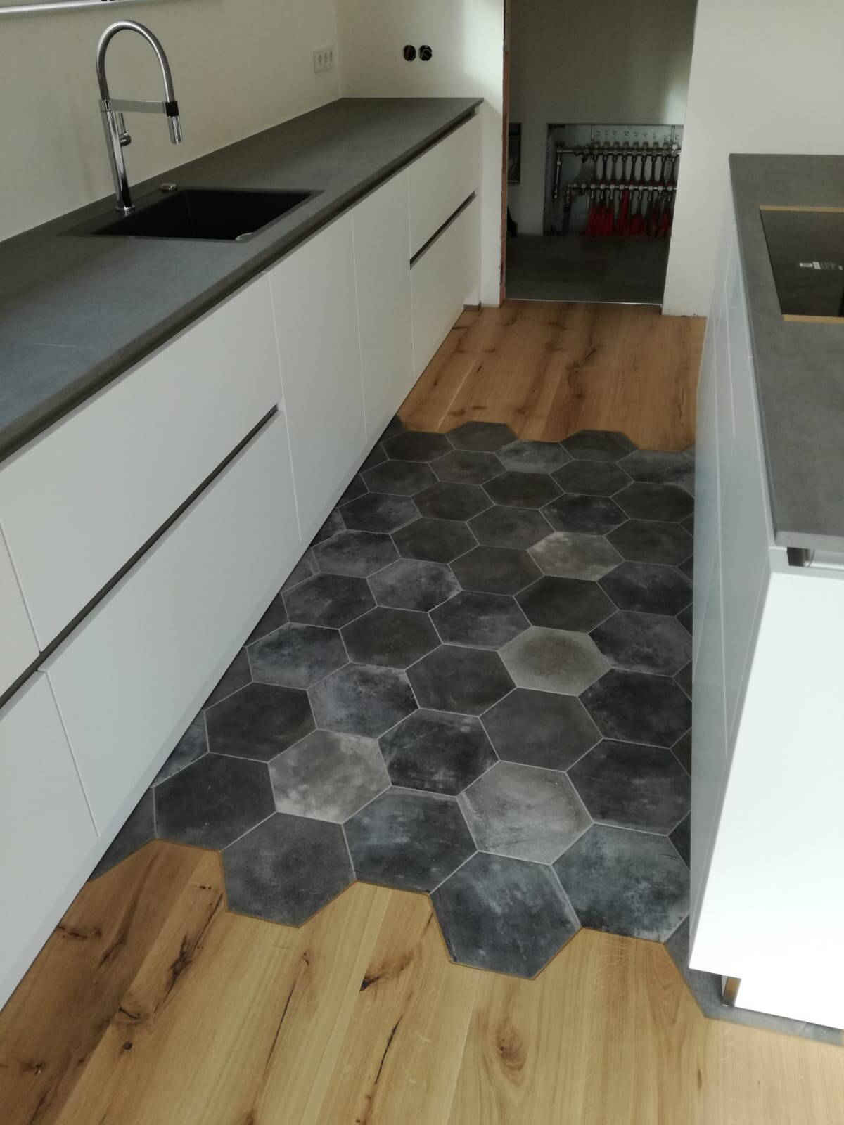 Moderne Küche mit weißen Unterschränken, grauer Arbeitsplatte, Spüle und hexagonalem Fliesenboden.