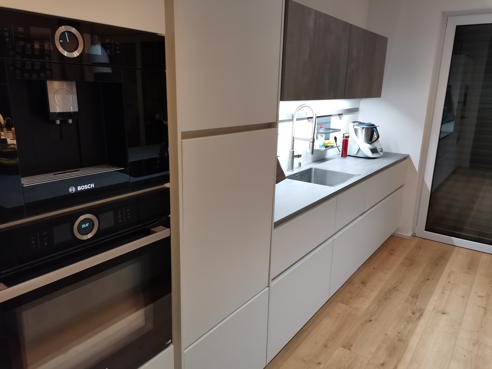 Moderne Küchenzeile mit Bosch-Backofen, Spüle, Thermomix und weißen Unterschränken.