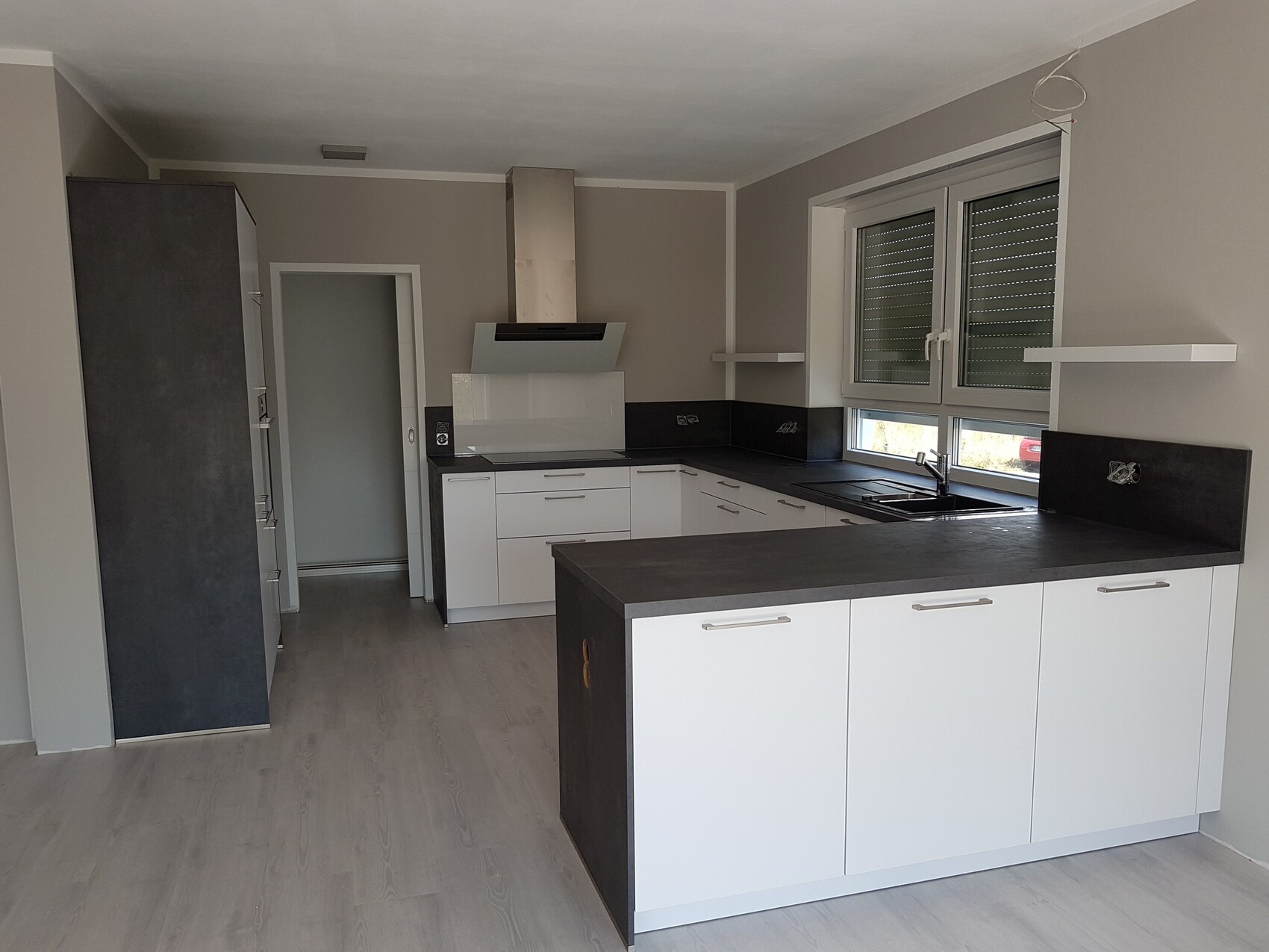 Moderne Küche mit Insel, weißen Unterschränken, dunkler Arbeitsplatte und Spüle am Fenster.