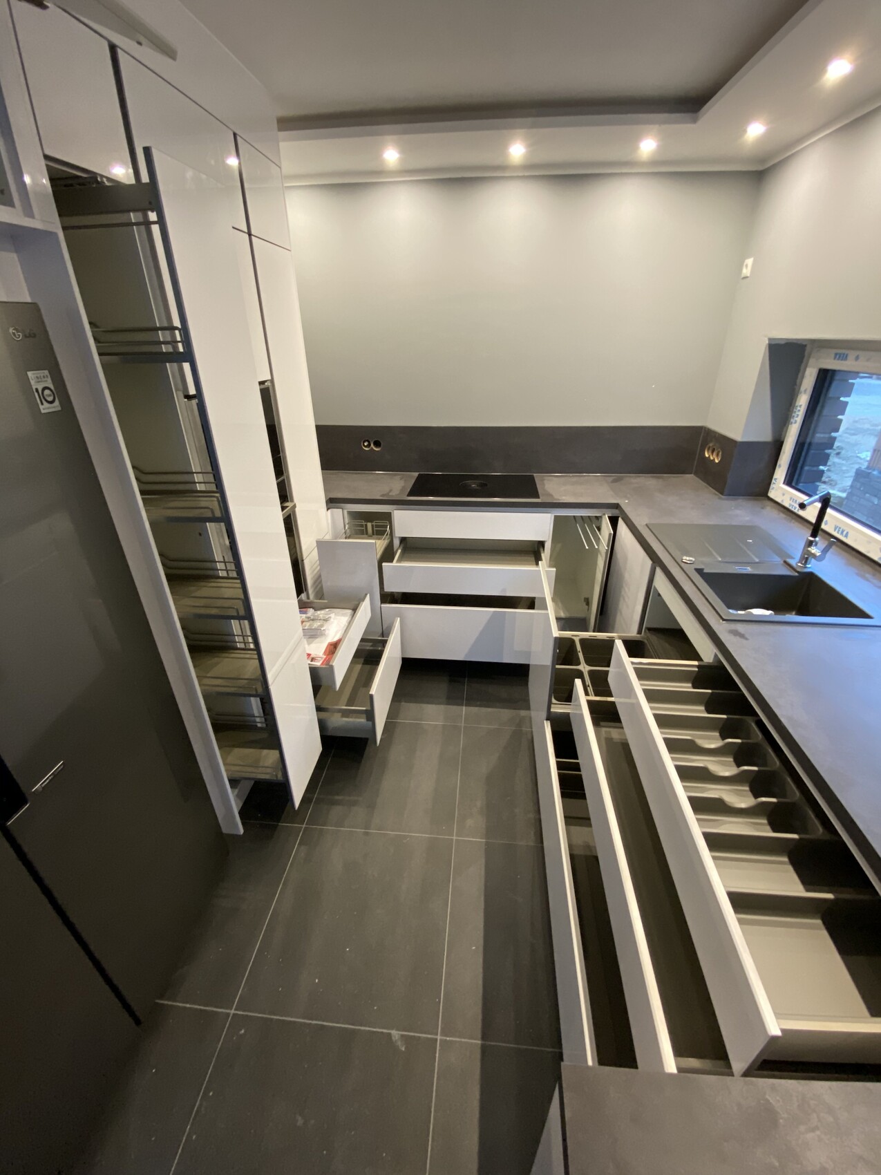 Moderne Küche mit weißen Hochglanzschränken, offenen Schubladen und dunkler Arbeitsfläche.