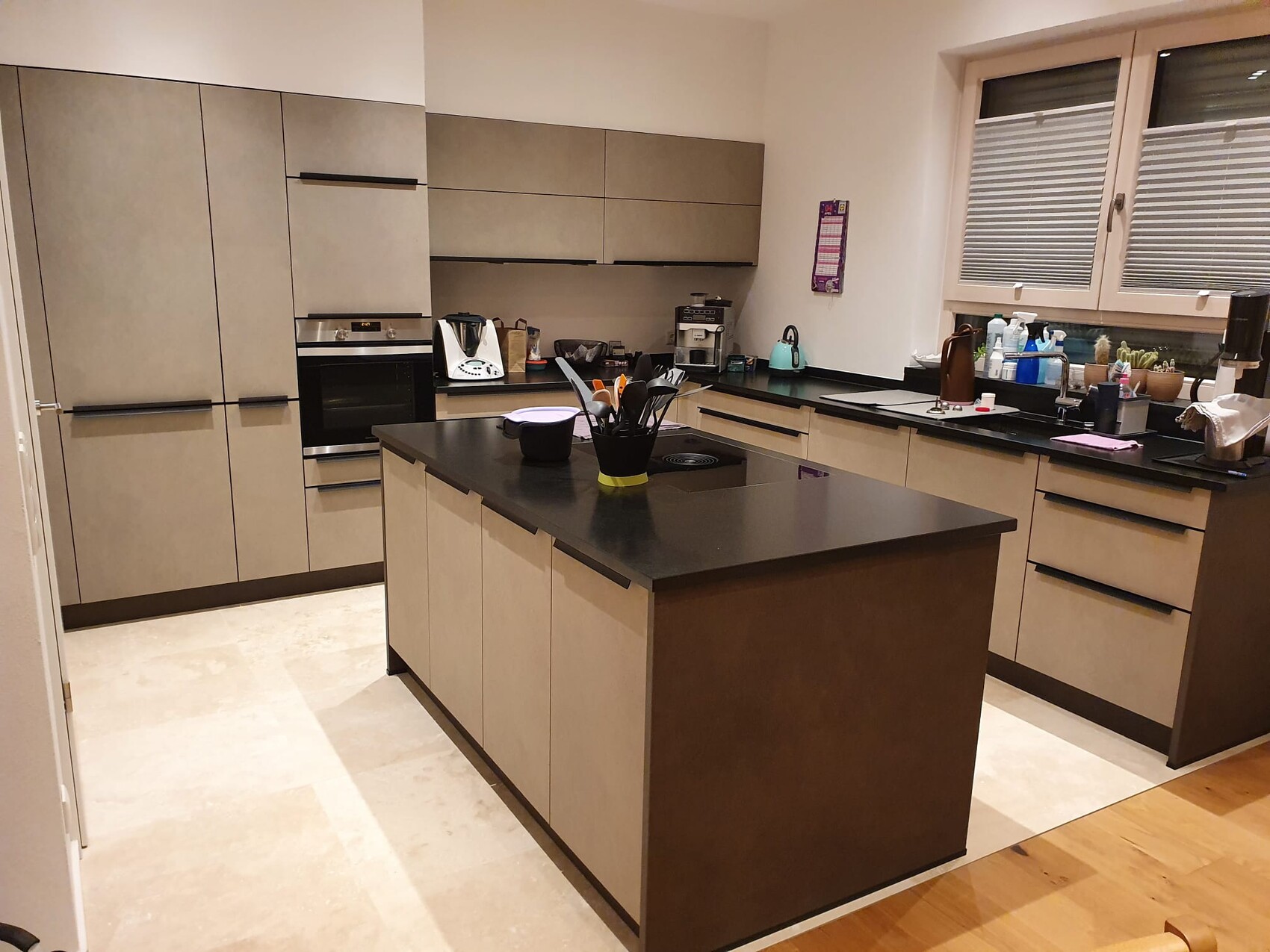 Moderne Küche mit zentraler Insel, graue Hängeschränke, Backofen und Spüle am Fenster.