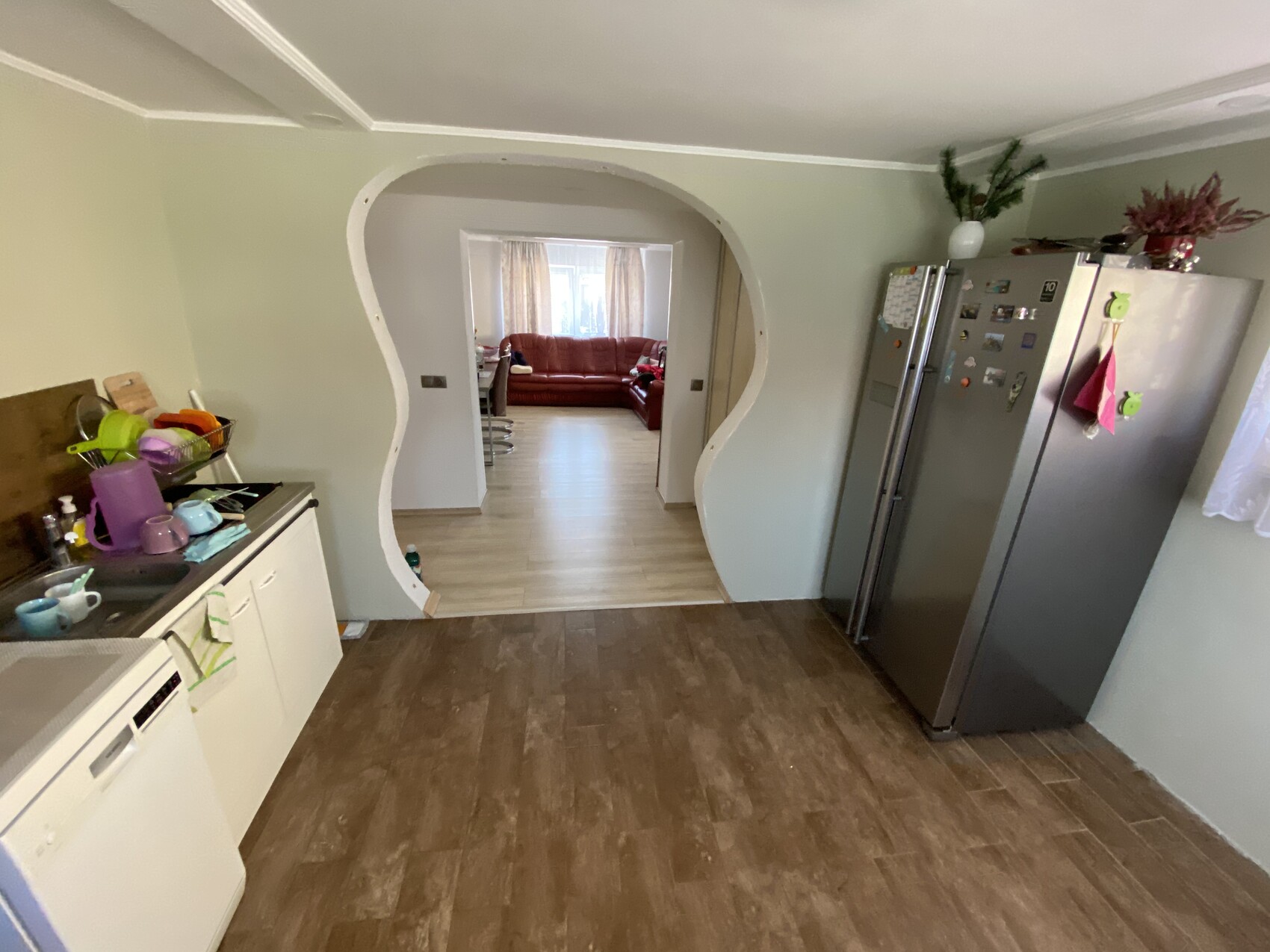 Küche mit geschwungenem Durchgang ins Wohnzimmer; rechts Kühlschrank, links Spüle.