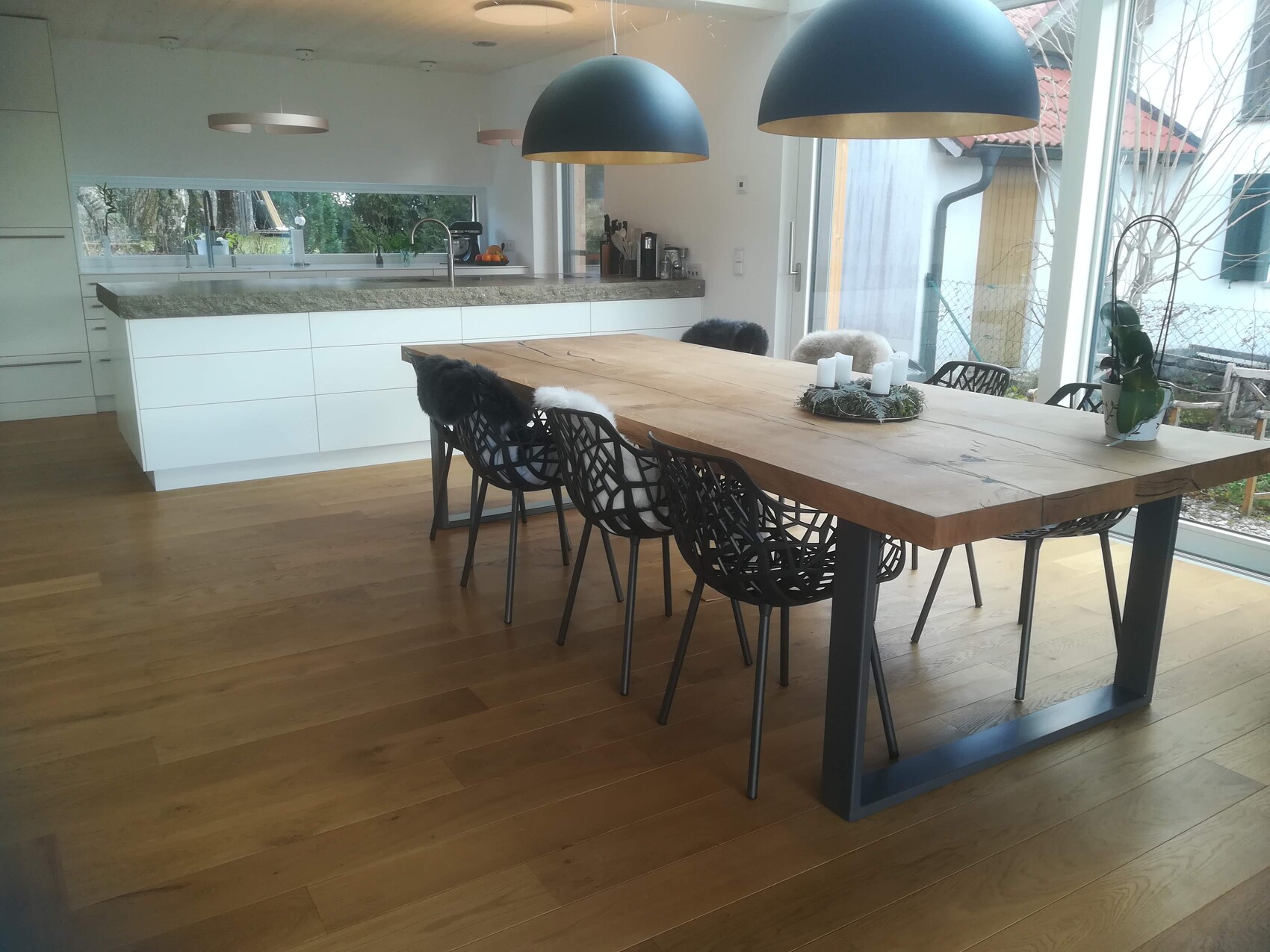 Offener Essbereich: massiver Holztisch, schwarze Stühle, Pendelleuchten, Blick nach draußen.