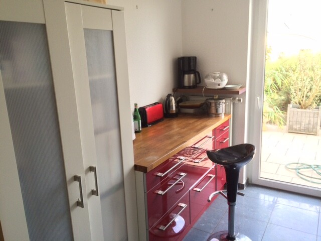 Küche mit roten Schränken, Holzarbeitsplatte, Barhocker und Glastür zur Terrasse.