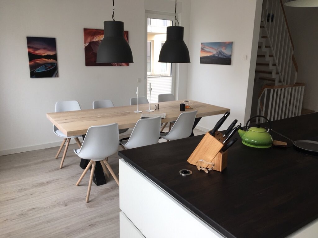 Helles Esszimmer: langer Holztisch mit weißen Stühlen, zwei Pendelleuchten, Kücheninsel.