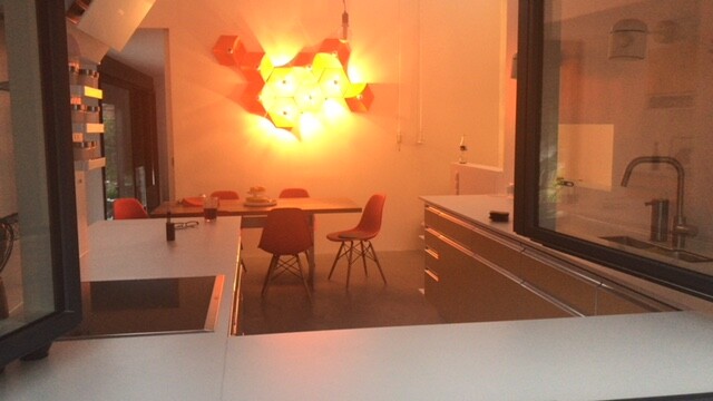 Moderne Küche mit Essbereich, weiße Arbeitsplatten, rote Stühle und orange Wandlampen