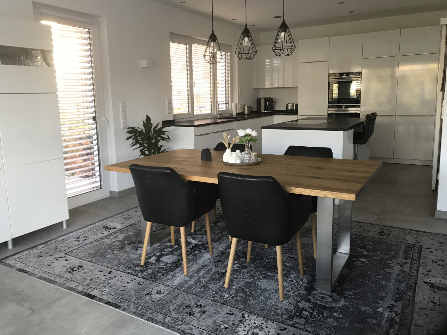 Moderne Küche mit Essbereich: weiße Fronten, Eichenholztisch, schwarze Stühle, Pendelleuchten