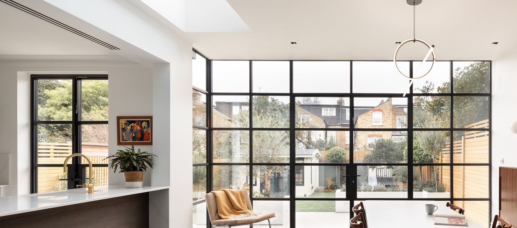 Moderne offene Wohnküche mit Insel, großen schwarzen Fensterrahmen und Gartenaussicht.