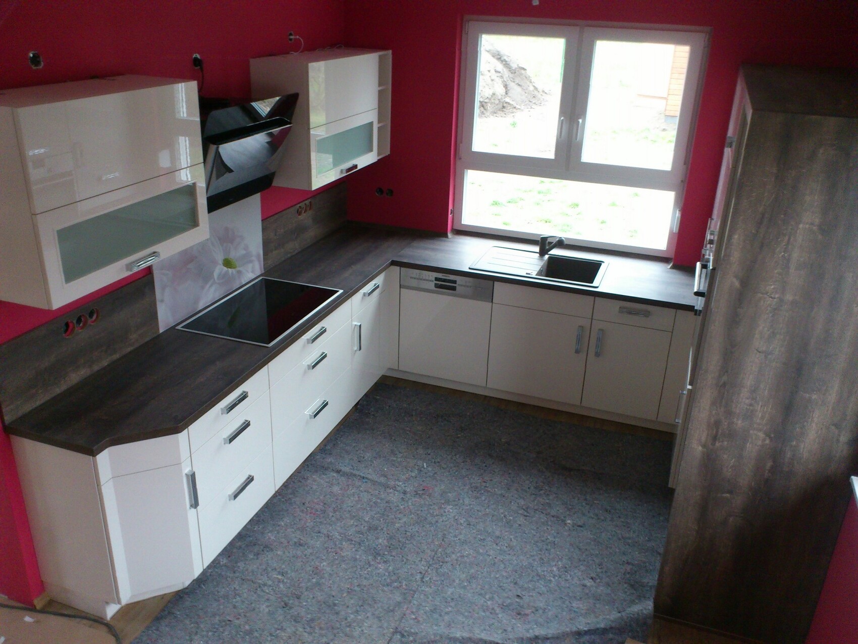 Küche mit rosa Wänden, weißen Schränken, dunklen Arbeitsplatten, Spüle am Fenster.