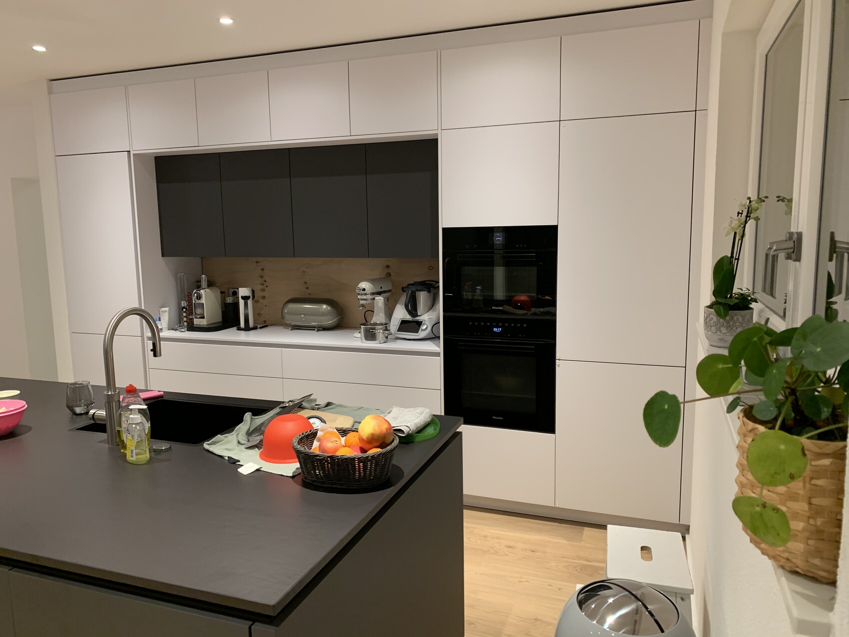 Moderne Küche mit weißen Schränken, grauen Oberschränken, Insel, Obstkorb und Backofen.
