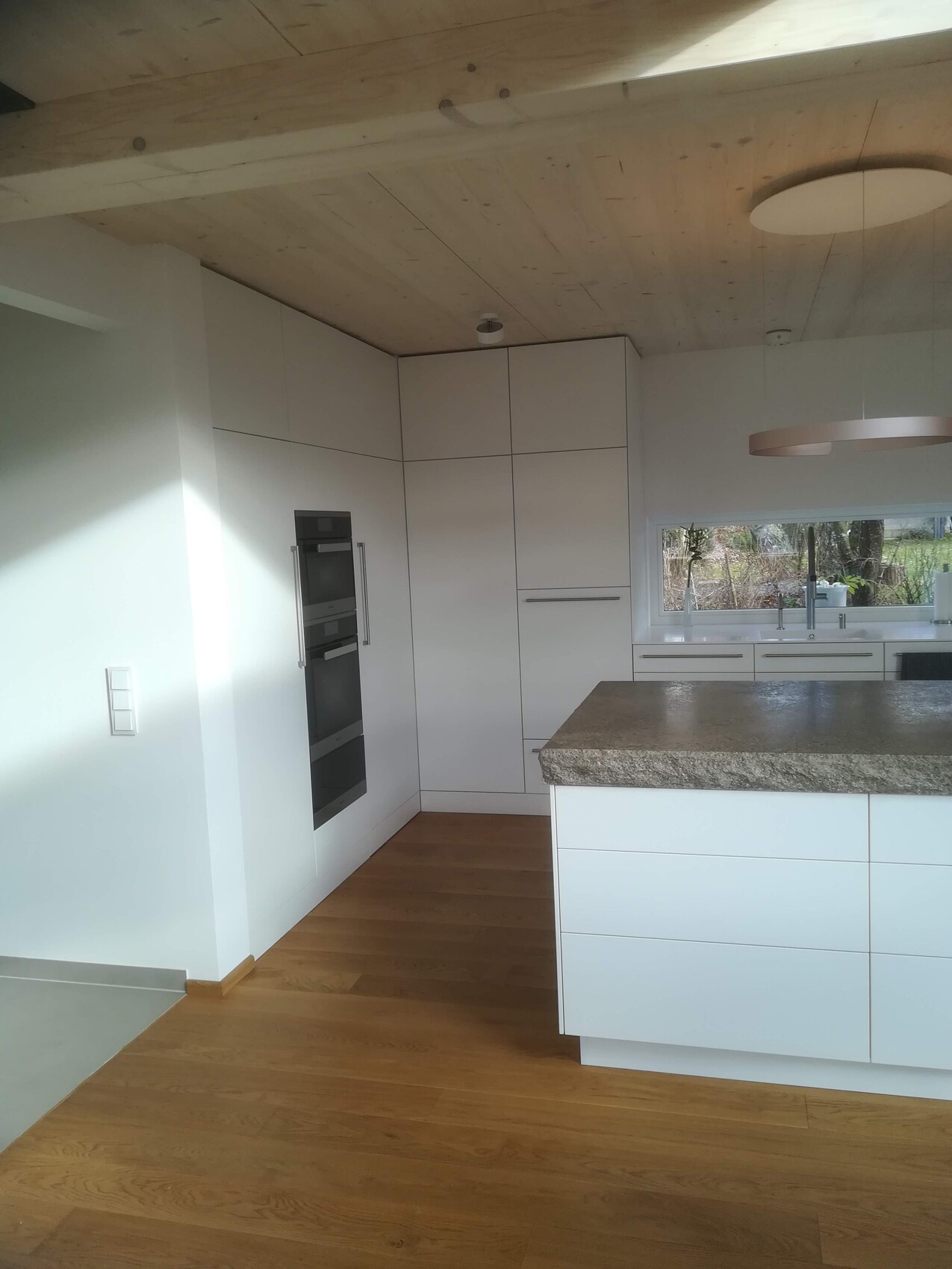 Moderne weiße Küche mit großer Insel, Granitplatte, integrierten Backöfen und Holzfußboden.