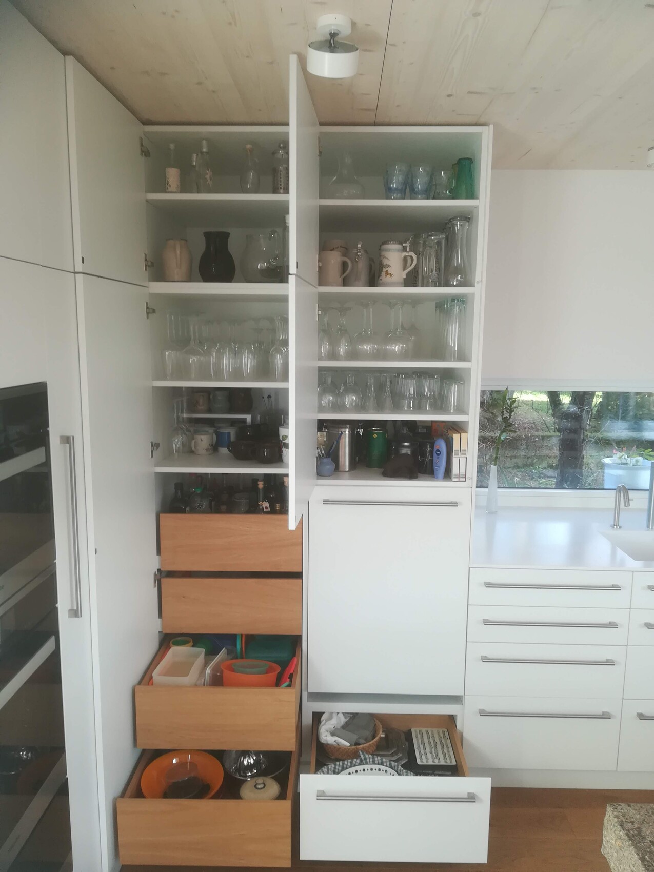 Offene Küchenschränke mit Gläsern, Tassen und Geschirr; darunter Schubladen mit Behältern.