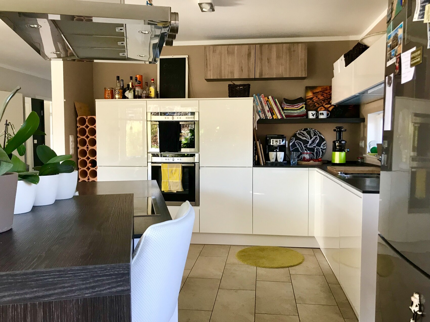 Moderne Küche mit weißen Hochglanz-Schränken, Doppelöfen, Insel, Pflanzen und Küchenutensilien.