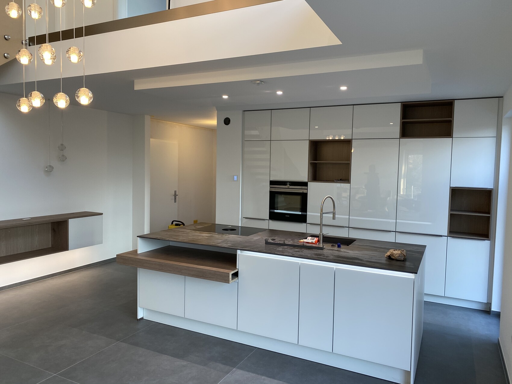 Moderne Küche mit weißen Fronten, Insel, Spüle, Backofen, Holzregale.