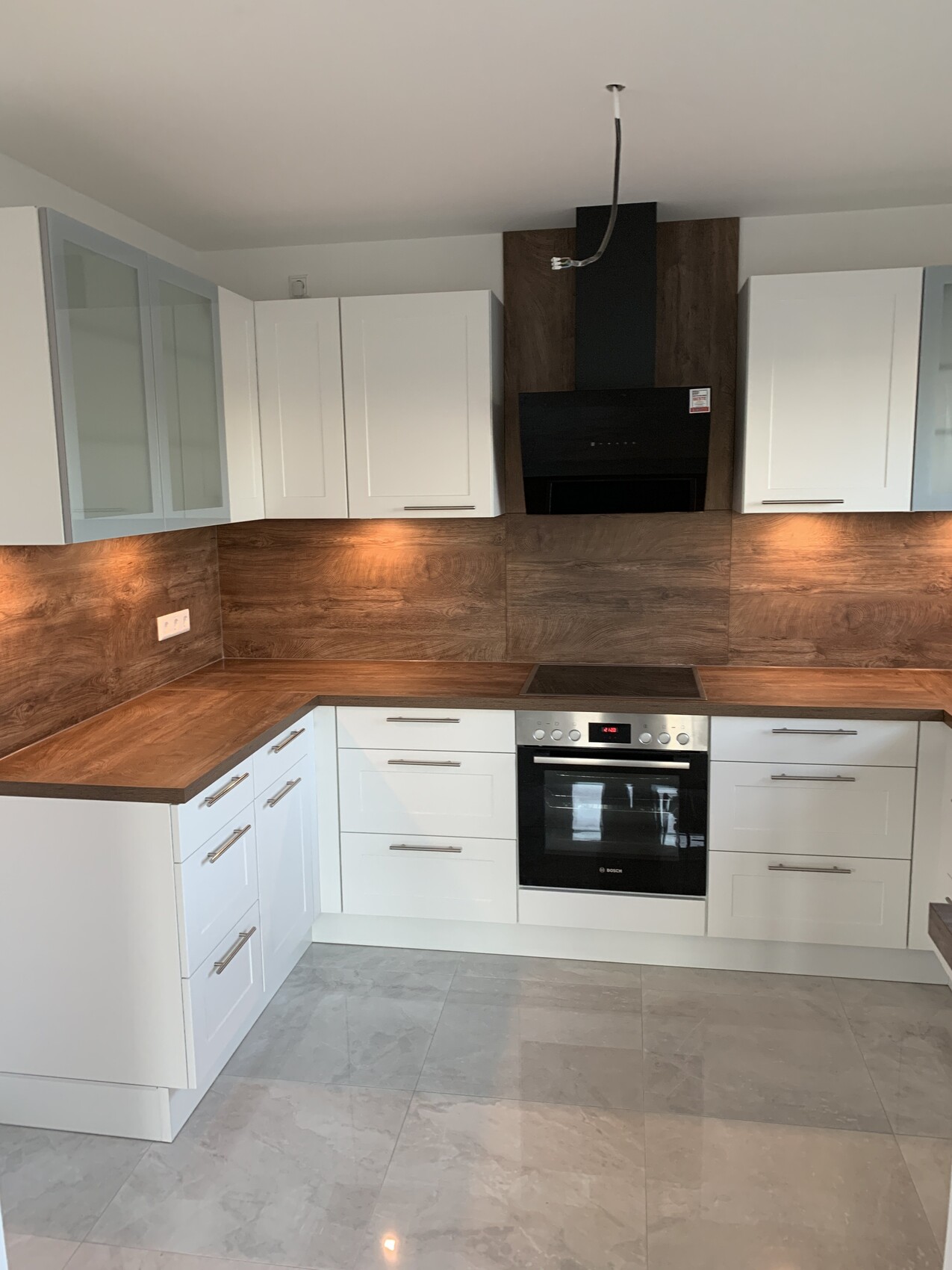 Moderne Küche mit weißen Schränken, Holz-Arbeitsplatten, Backofen mittig und dunklem Dunstabzugshaube
