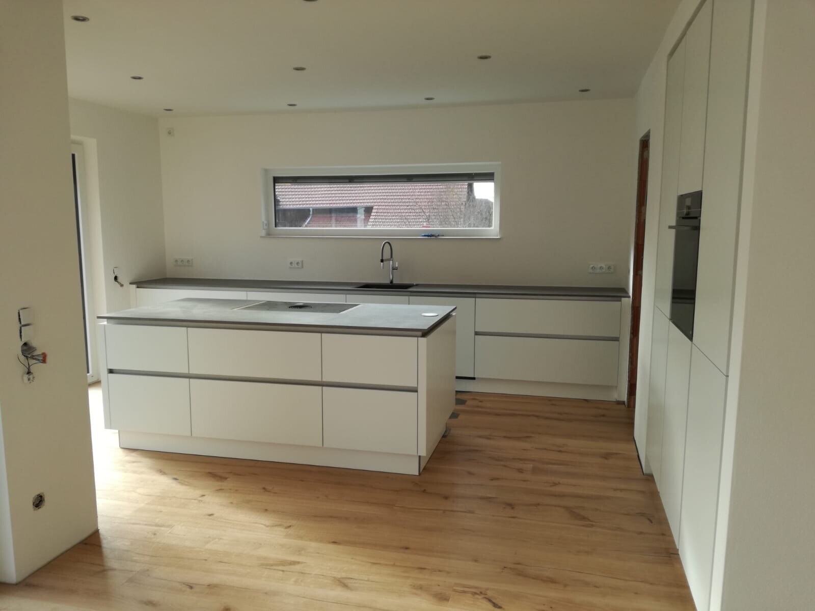 Moderne weiße Küche mit Insel, grauen Arbeitsplatten, Spüle und Holzboden.