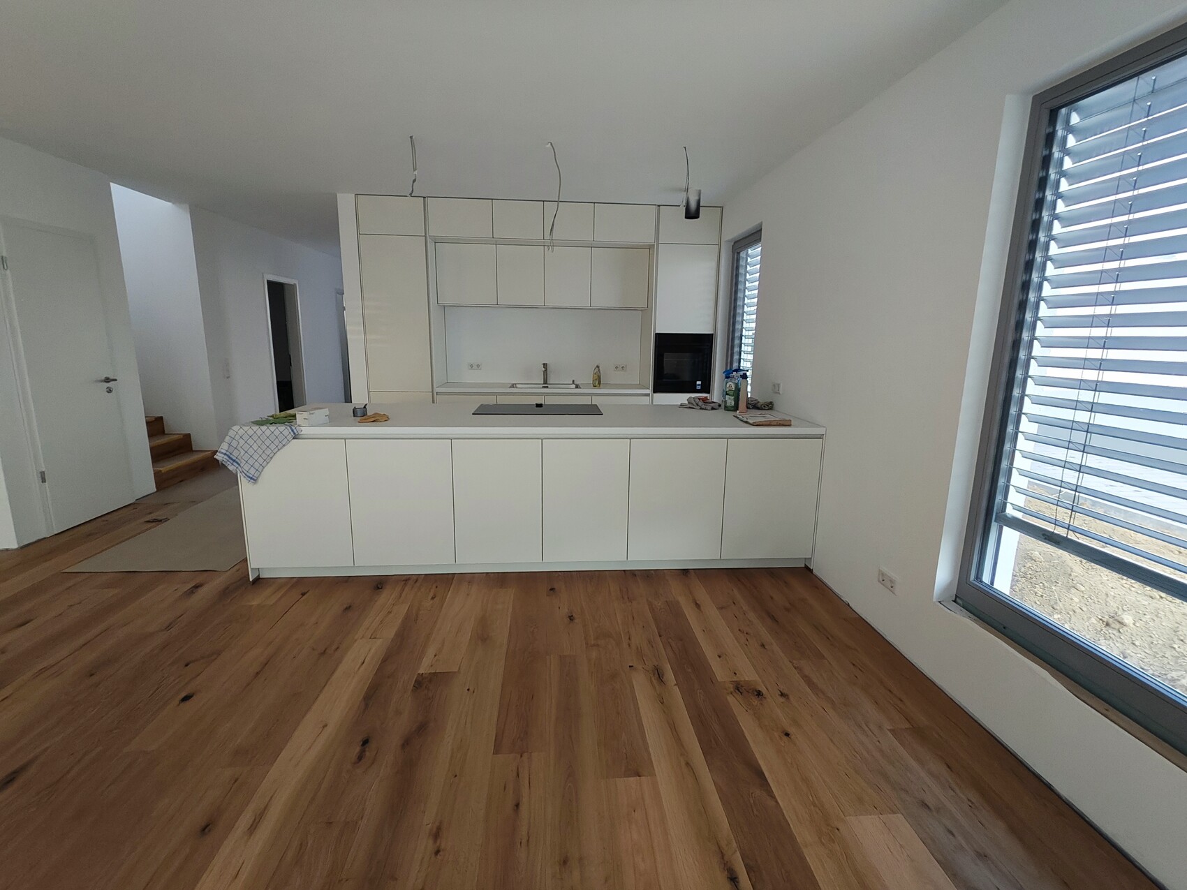 Moderne weisse kuechenzeile mit insel, grossen fensterfront, holzboden, bauarbeiten im hintergrund