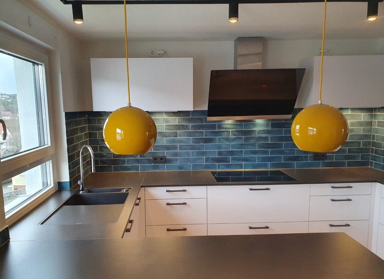 Moderne Küche mit blauen Fliesen, Induktionskochfeld, Dunstabzugshaube, gelben Pendelleuchten