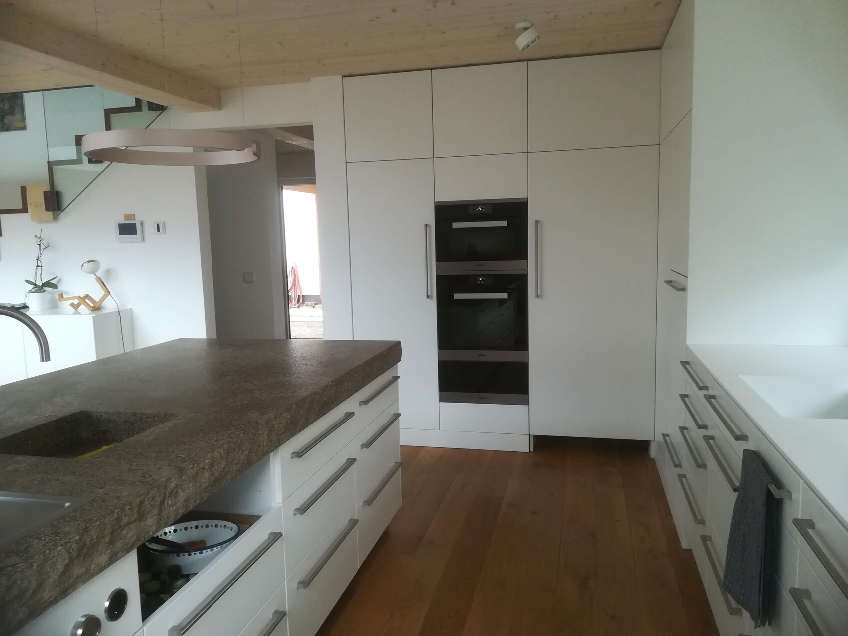 Moderne weiße Küche mit Insel, Holzboden und integrierten Backöfen.