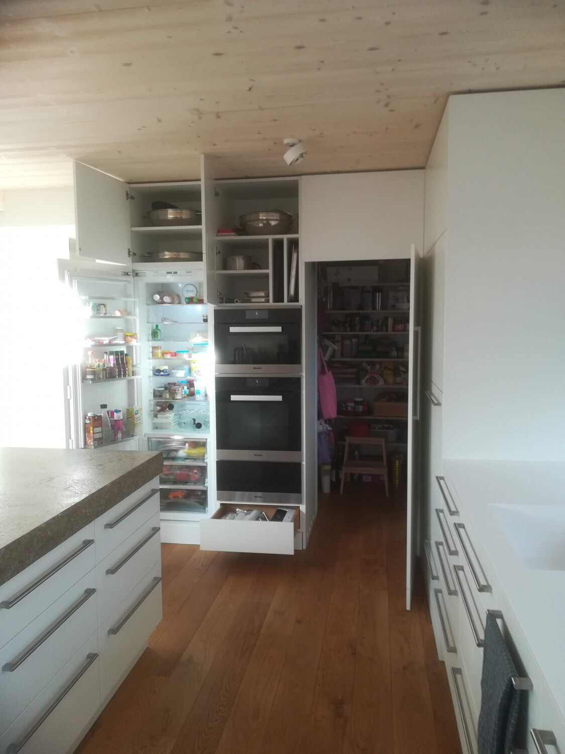 Moderne Küche mit offenen Vorratskammern, Einbau-Backöfen, Kühlschrank und Holzboden.