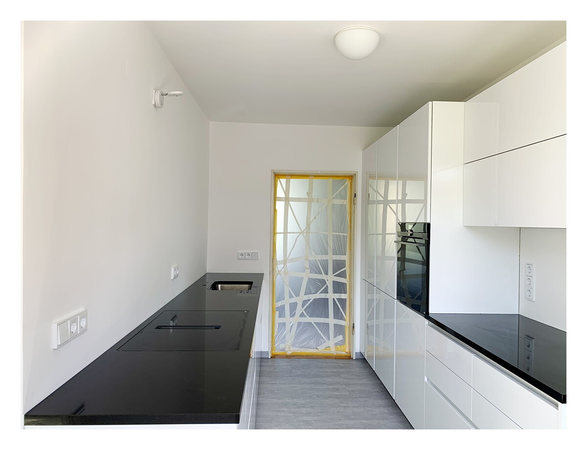 Moderne Küche mit weißen Schränken, schwarzer Arbeitsplatte und eingebautem Ofen.