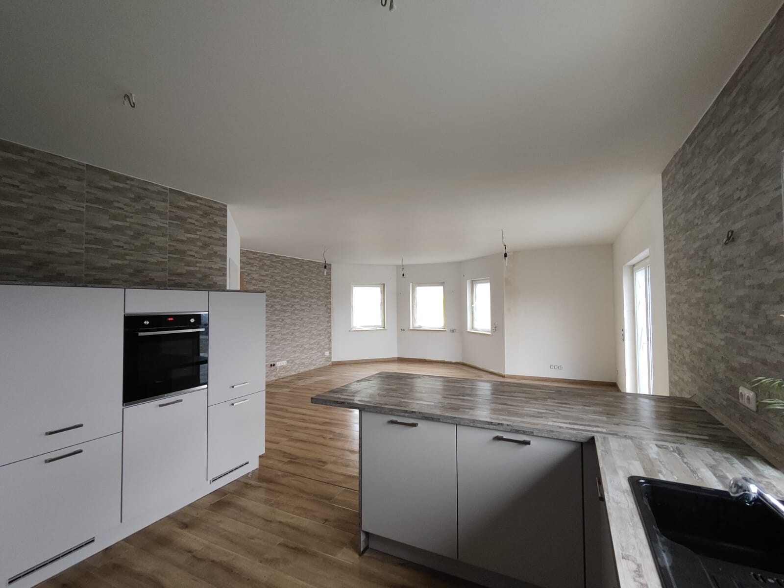 Moderne offene Küche mit grauen Schränken, Insel, Holzfußboden, leere Wände und mehrere Fenster.