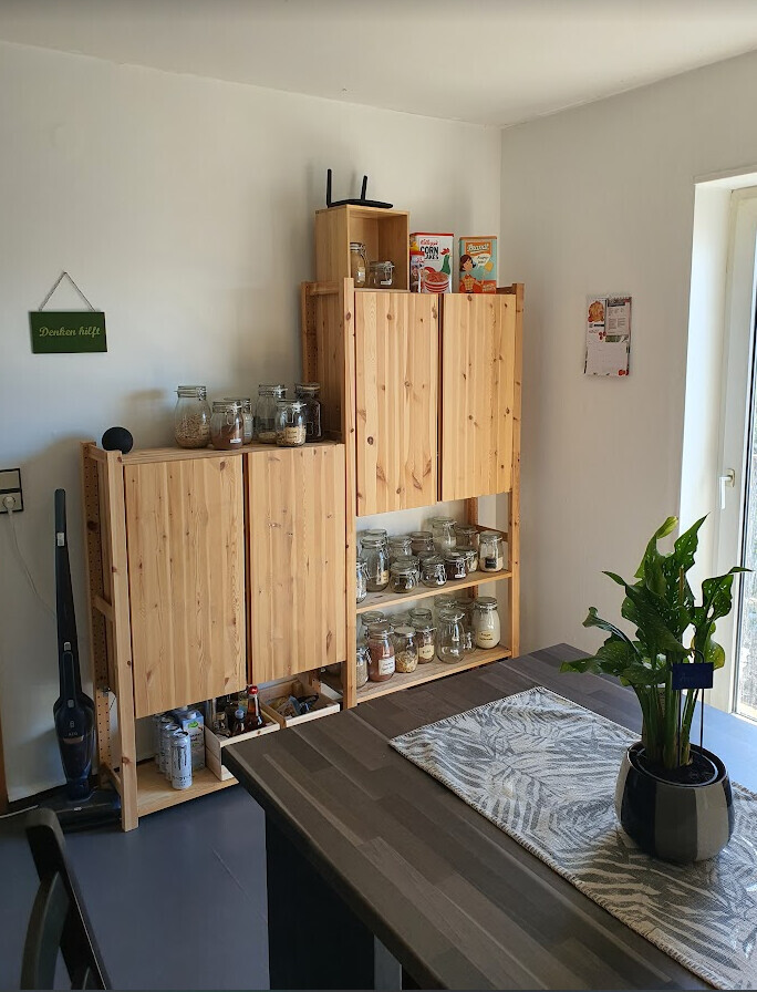 Holzregale mit Gläsern, Vorratsdosen und Cerealienboxen; Esstisch mit Pflanze.