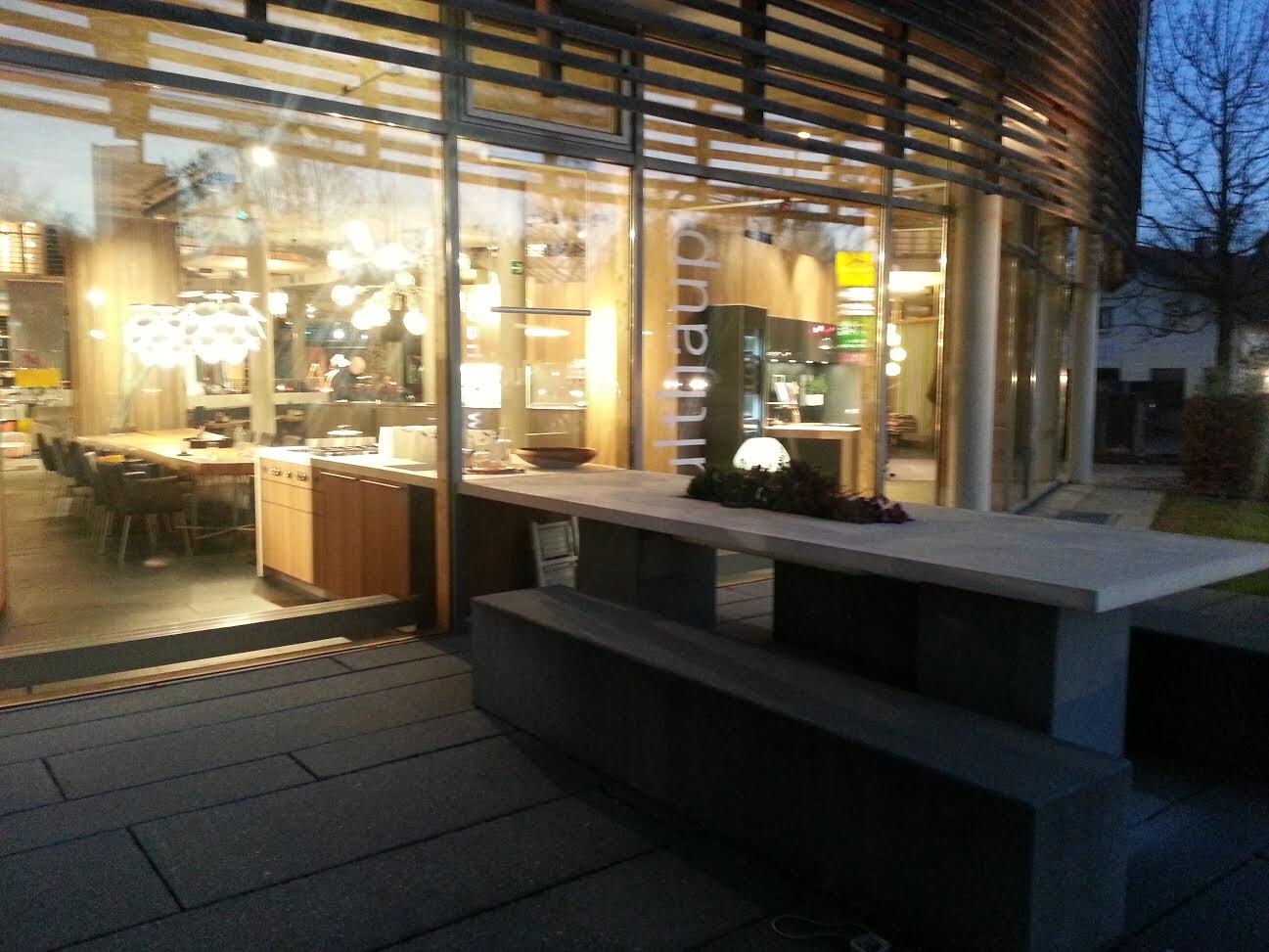 Moderne Küchen-Showroom-Szene mit Esstisch und Glasfronten bei Abendlicht