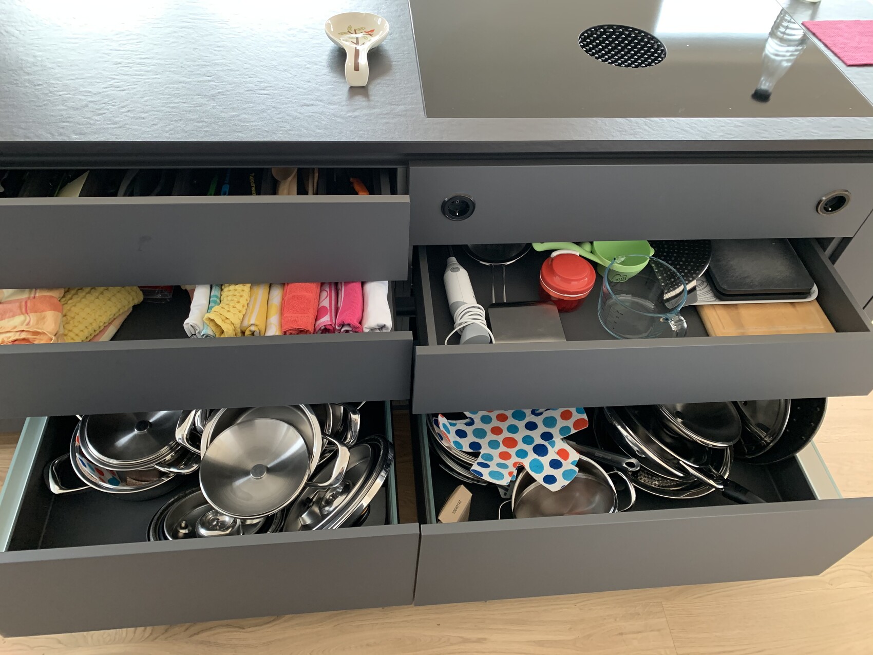Offene Küchenschubladen mit bunten Handtüchern, Gläser, Deckeln, Töpfen und Pfannen