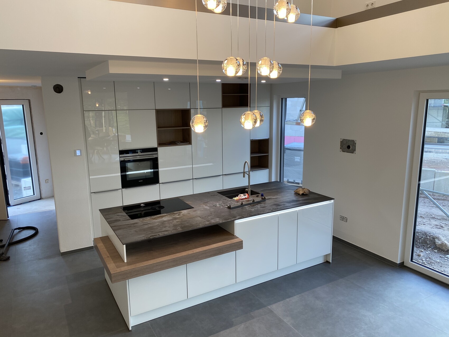 Moderne Küche: weiße Schränke, Insel mit Spüle, Backofen, Pendelleuchten.