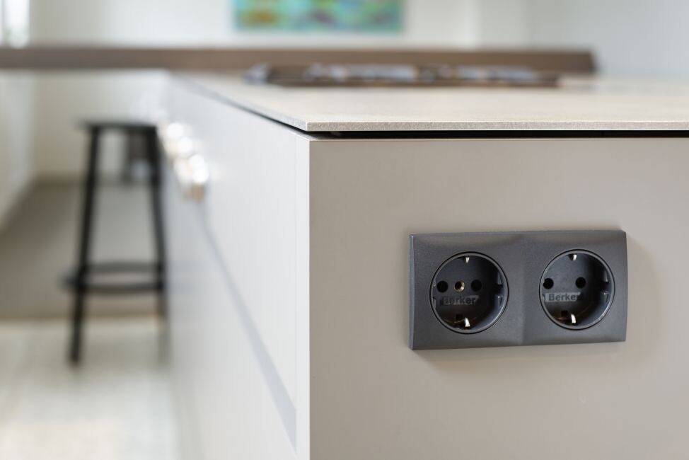 Nahaufnahme einer grauen Doppel-Schuko-Steckdose in der Kücheninsel, Hintergrund unscharf.