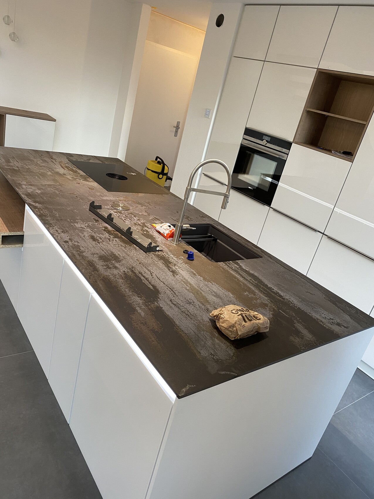 Moderne weiße Kücheninsel mit dunkler Arbeitsplatte, Spüle, Armatur und Werkzeug auf der Fläche.