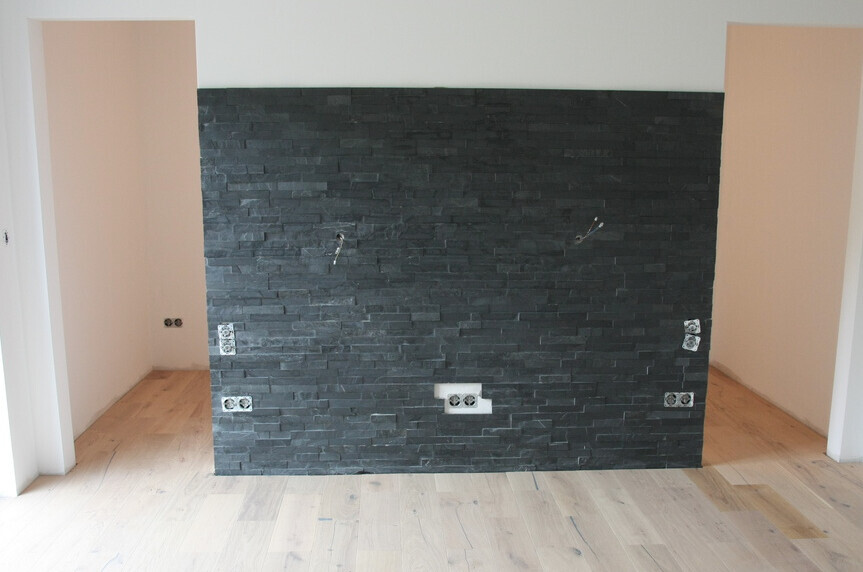 Trennwand aus dunklen Steinplatten mit Steckdosen und Kabelauslässen in hellem Raum.